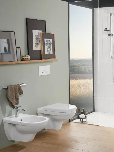 Modernes Bad mit WC, Bidet, Waschbecken und Dusche aus der Kollektion O.novo Das moderne Bad mit beigefarbenen Fliesen und pastellfarbenen Wänden ist mit einem O.novo-Wand-WC, einem Bidet, einem Waschbecken mit Spiegel und einer bodengleichen Dusche ausgestattet. Die Regale sind mit gerahmten Kunstwerken und Toilettenartikeln bestückt. Auf dem Boden stehen Körbe.