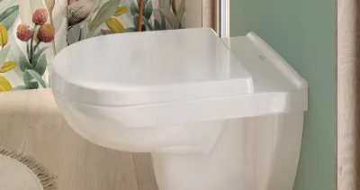 O.novo-WC mit Blümchentapete Modernes Badezimmer mit wandmontiertem O.novo-WC, hellgrünen Wänden und geblümter Tapete. Neben dem WC befindet sich ein kleiner runder Tisch mit gefalteten Handtüchern.