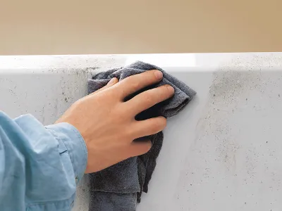 Nettoyage d’une baignoire en Quaryl blanc Une personne vêtue d’une chemise bleue enlève la saleté d’une baignoire en Quaryl blanc à l’aide d’un chiffon foncé.