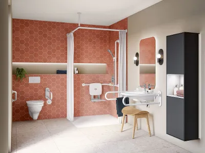 Barrierefreies modernes Badezimmer mit Badkeramik der ViCare Kollektion in Weiß und Sicherheitsgriffen Barrierefreies Badezimmer mit orangefarbenen, sechseckigen Fliesen, einer ebenerdigen Dusche mit Haltegriffen und Klappsitz, einem wandmontierten Waschbecken mit Sicherheitsgeländern, einem hinterleuchteten Spiegel, einer Toilette mit Haltegriffen und Stauraumeinheiten.