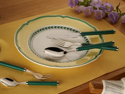 A dining room set with the Villeroy & Boch Play! collection, featuring a decorative plate, cutlery with green handles and a yellow placemat on a wooden table with purple flowers in the background.
