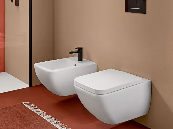 Venticello Bidet und WC Modernes Badezimmer mit wandmontiertem Bidet und WC, einem Regal mit gefalteten Handtüchern und einer Duschkabine aus Glas. Der Raum hat braune Wände und einen roten Boden mit einem gemusterten Teppich.