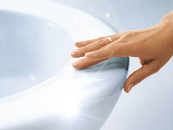Hand berührt CeramicPlus Toilette Nahaufnahme einer Hand mit einem goldenen Ring, die den Rand eines weißen, glänzenden Keramik-WCs berührt.