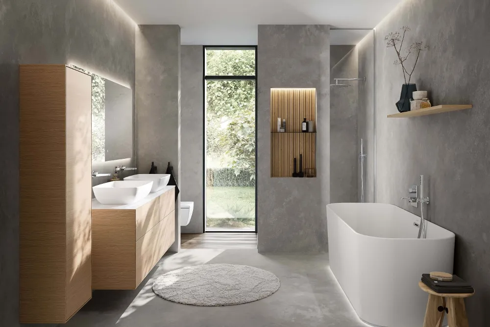 Minimalistisches Badezimmer mit Villeroy & Boch 'Finion' Badewanne, 'Finion' Waschtischunterschrank und zwei 'Artis' Waschbecken. Das schlichte Design kombiniert natürliche Holzelemente mit modernen grauen Wänden und einer großen Fensterfront für ein helles, ruhiges Ambiente.