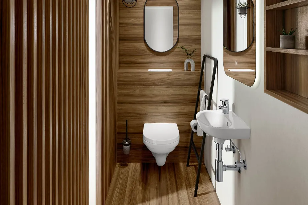 Modernes Badezimmer mit Holzvertäfelung, wandhängendem WC mit ovalem Spiegel, kleinem weißen Waschbecken mit großem Spiegel und Regal mit Utensilien. Rechts steht eine Leiter mit schwarzem Rahmen als Dekoration und Ablage.