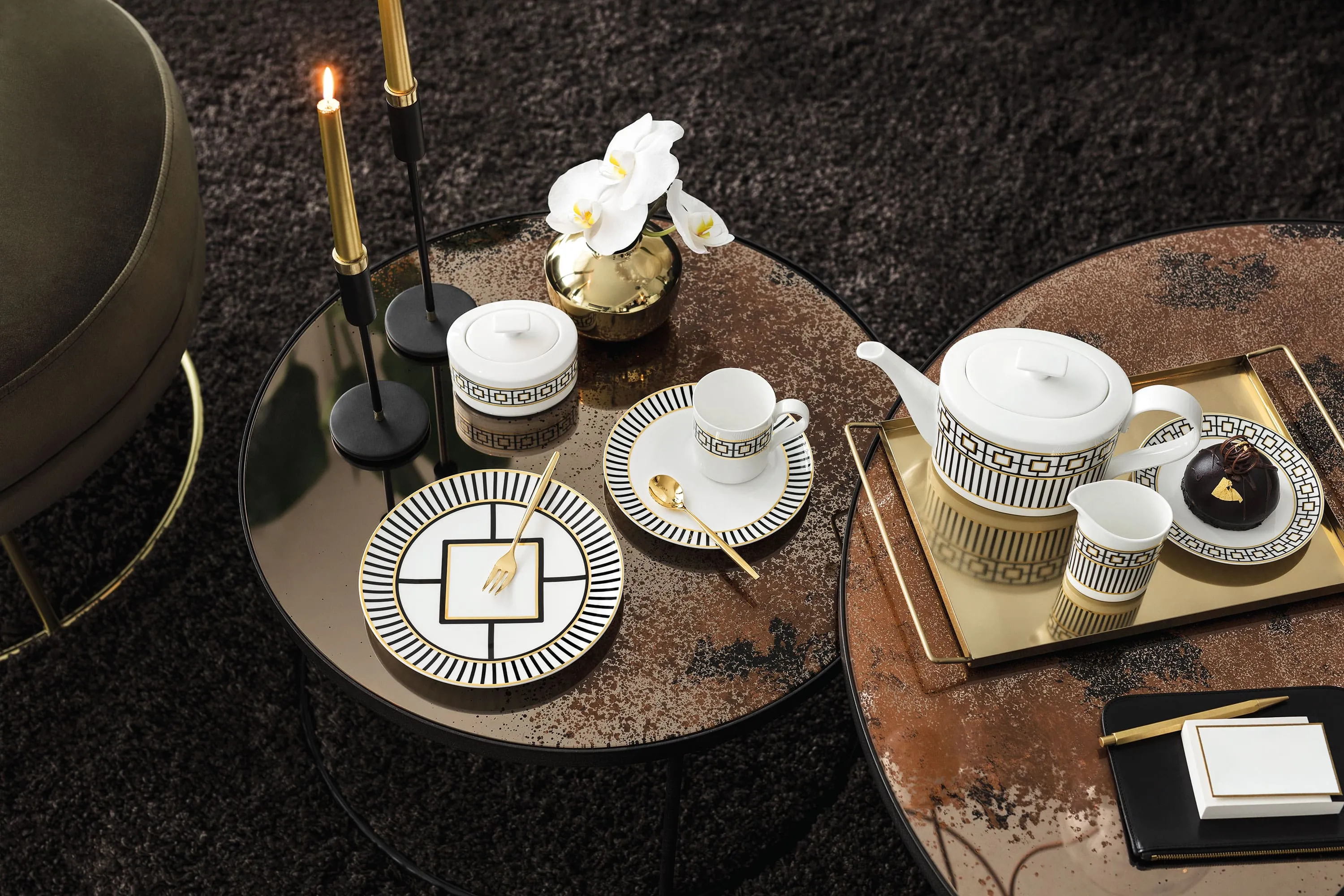 MetroChic tea set on a round table with gold accents, accompanied by orchids, candles and small snacks.