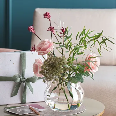 Rose Garden Vase mit Rosen Eine Rose Garden Vase mit rosa Blumen und einem Geschenk auf einem Tisch.