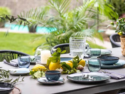 Esstisch im freien mit Lave und Zitrusfrüchten Esstisch im Freien mit Lave Geschirr, Gläsern, Kerzen und frischen Zitrusfrüchten als Tafelaufsatz mit Blick auf einen Pool.