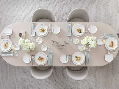 De la vaisselle Afina avec des couverts de table Piemont et un délicieux repas servi sur une table de salle à manger beige Une table de salle à manger élégante, dressée pour six personnes, avec de la vaisselle Afina blanche, des couverts de table Piemont et un délicieux repas.