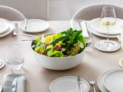 Un plat creux blanc Afina avec de la salade Un grand plat creux de service Afina de Villeroy & Boch, rempli de salade, sur une table dressée.