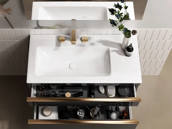 Venticello Waschbecken mit offenem Waschbeckenschrank Ein moderner Waschbeckenschrank mit einer offenen Schublade, in der Pflegeprodukte aufbewahrt werden. Auf der Ablagefläche steht eine kleine Blumenvase.