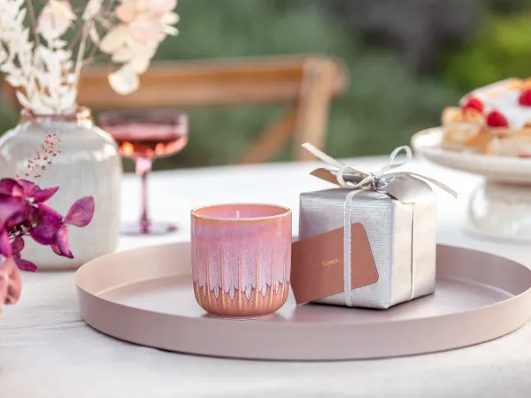 Rosa Perlemor Duftkerze als Geschenk Duftkerze aus der Kollektion von like. by Villeroy & Boch als Geschenk auf rundem Tablett mit silberner Geschenkbox im Hintergrund und rosa Orchideen im Vordergrund.
