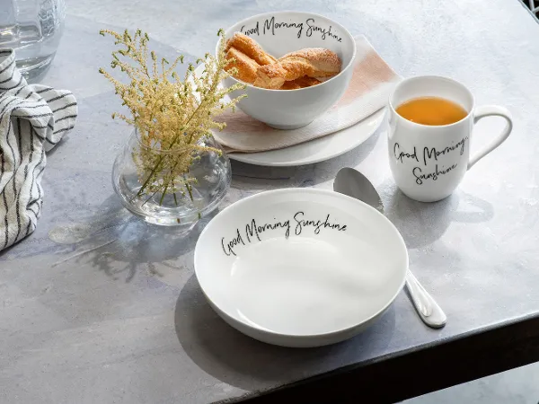 Statement Tasse, Teller und Bol „Good Morning Sunshine“ auf einem Tisch Ein Tisch mit einer Statement Tasse Kaffee und einem Statement Teller mit Croissants von Villeroy & Boch.
