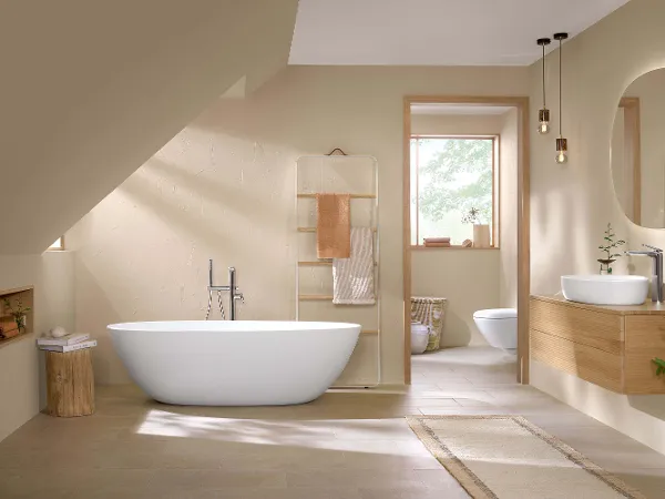 Freistehende Antao Badewanne mit Aufsatzwaschtisch und Armaturen in modernem Badezimmer Modernes Badezimmer-Interieur mit freistehender Badewanne, Holzwaschtisch mit Aufsatzwaschbecken, Toilette, runden Spiegeln und beigen Wänden, mit natürlichem Licht, das durch eine offene Tür einfällt.