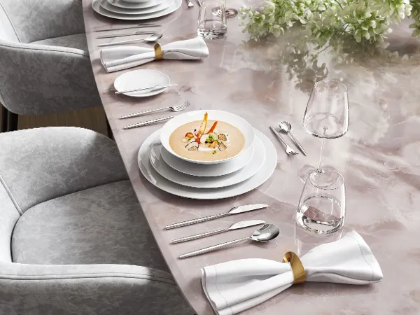 Eleganter Esstisch mit Suppe in einer weißen MetroChic Tellern Eleganter Esstisch mit Suppe in einer weißen MetroChic Tellern, Gläsern und Besteck auf einem Marmortisch, begleitet von Blumen