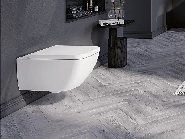 Toilette in weiß der Kollektion Collaro Ein modernes Badezimmer mit wandhängender weißer Toilette von Villeroy & Boch, dunklem Regal mit Dekorationen und einem kleinen Beistelltisch mit Pflanze. Der Raum hat graue Wände und einen Boden mit Fischgrätenmuster.