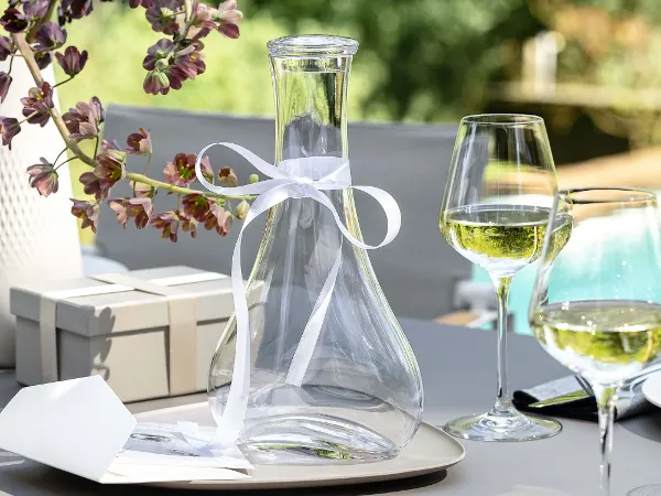 Purismo Weinkaraffe mit Weingläsern auf einem Tisch Eine elegante Purismo Weinkaraffe mit weißer Schleife und Weingläser auf einem Tisch.