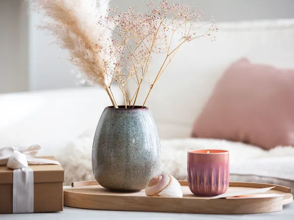 Holztablett mit Lave Vase und Perlemor Kerze Holztablett auf dem eine Lave Vase und eine Perlemor Kerze mit getrockneten Blumen stehen, neben einem verpackten Geschenk.