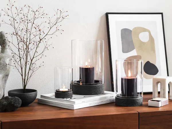 Manufacture Windlichter auf hölzernem Sideboard Eine moderne Wohneinrichtung mit einem hölzernen Sideboard und Trockenblume mit drei Manufacture Windlichtern.