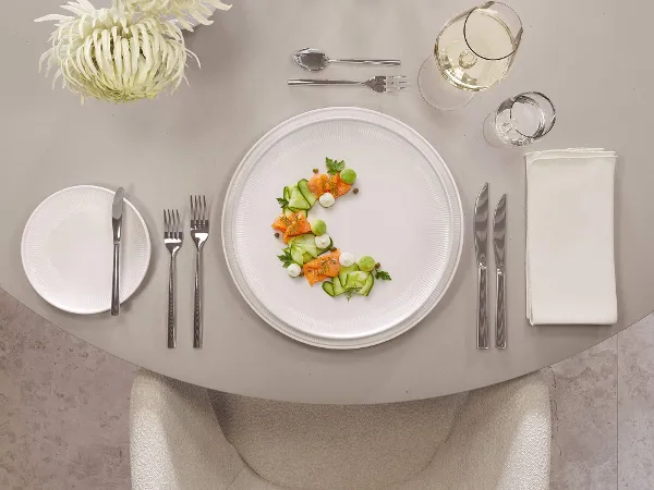 Afina Tellern mit Lachs-Gurkensalat auf einem eleganten Esstisch Eleganter Esstisch mit Lachs-Gurkensalat auf Afina Tellern, begleitet von Wein in La Divina Gläsern und Piemont Besteck.