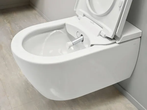 ViClean-I200 Dusch-WC mit ausgefahrenem Duschkopf Eine Nahaufnahme einer modernen wandmontierten Dusch-Toilette mit geöffnetem Deckel und einem aus der Schüssel austretenden Wasserstrahl.