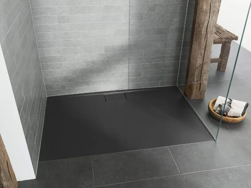 Eine moderne ebenerdige Dusche mit schwarzem Boden, grau gefliesten Wänden, einer Glastrennwand und einem Holzbalken. In der Ecke ist ein Holzhocker mit einem Korb mit Handtüchern und Seife zu sehen.
